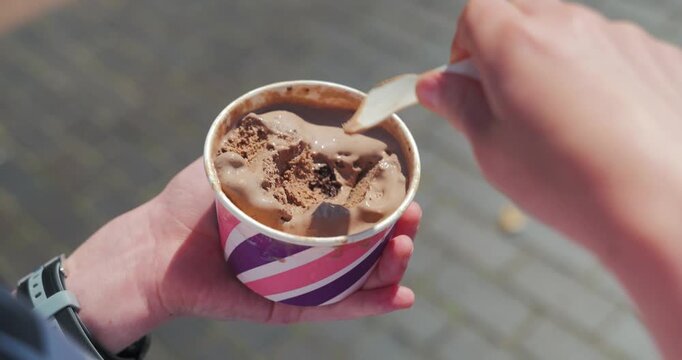 Close up of a childs hands eating chocolate ice cream from a cup outdoors on a sunny day