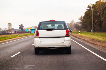 Fototapeta premium White color family car minivan or station wagon traveling on asphalt road through rural landscape under overcast sky daytime autumn season