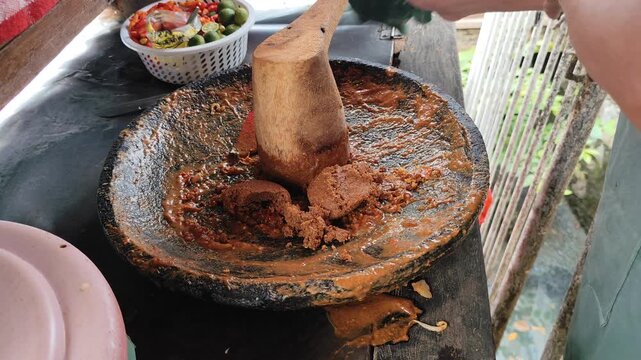 gado-gado indonesian street food vendor adding brown sugar and liquid to peanut sauce on stone mortar close up