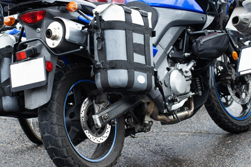 Fototapeta premium Adventure touring motorcycle parked on wet asphalt road surface. Close up view of rear wheel, exhaust pipe, taillight, and luggage bags for long distance travel.