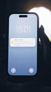 Vertical video. Smartphone Showing Shelter in Place Emergency Notification Inside Dark Tunnel With Bright Backlight, Cinematic Crisis Scene About Public Safety and Survival