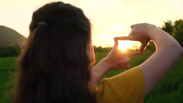 Preteen girl making frame gesture at amazing warm sunset in beautiful summer park. Concept of seeing world as different. Business planning. Child shows fingers frame symbol. Selective focus