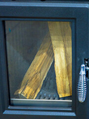 Fototapeta premium Modern Black Cast Iron Wood Burning Stove with Chopped Logs Inside Glass Door