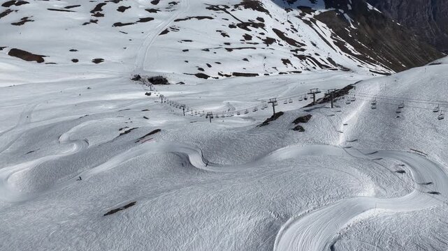 Spring sunshine over Val d'Isere ski resort in the French Alps, snowboarders riding a snowboard cross course on soft snow, alpine scenery with mountains, blue sky in sunny spring. Tignes, France