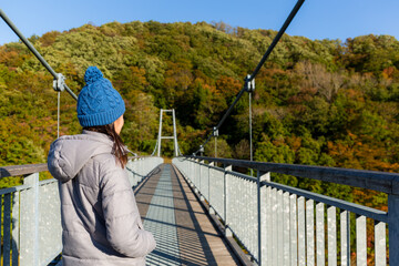 Naklejka premium Woman walking on suspension bridge in mountain forest