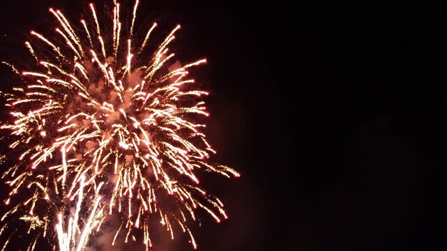Vibrant red and orange fireworks exploding in the night sky with smoke