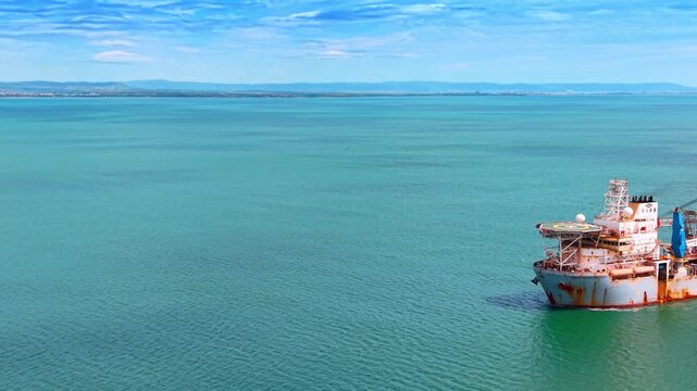 Aerial close up of rusty industrial drillship bow with helipad. High angle view of an offshore drilling vessel bow showing helipad and rusty hull in turquoise sea water.