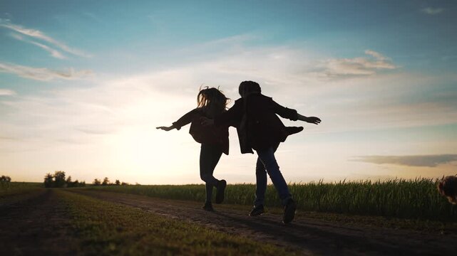 Girls run on dirt road. Small dog runs beside happy child. Dark silhouette against bright sunset. Carefree summer sunset brings true freedom. Open nature surrounds running girl and active dog.