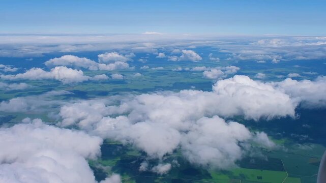 Aerial view from airplane of green meadows. White cumulus clouds in blue sky. Travel, freedom concept. Aviation, transportation