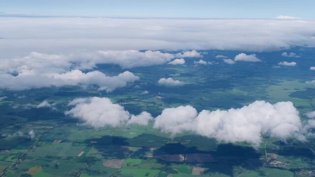 Aerial view from airplane of green meadows. White cumulus clouds in blue sky. Travel, freedom concept. Aviation, transportation