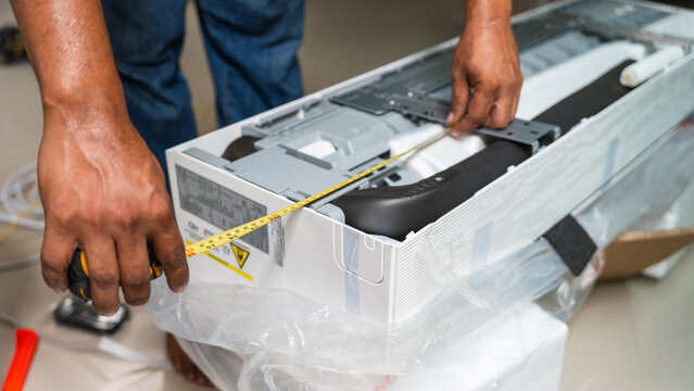 Technician measuring indoor air conditioner unit for installation, HVAC worker using a tape measure on a new air conditioner, Measuring dimensions for wall-mounted air conditioning unit installation