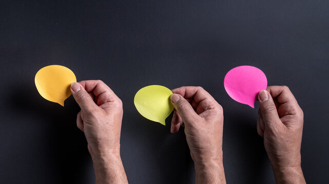 Three male hands holding colorful blank speech bubbles on dark background