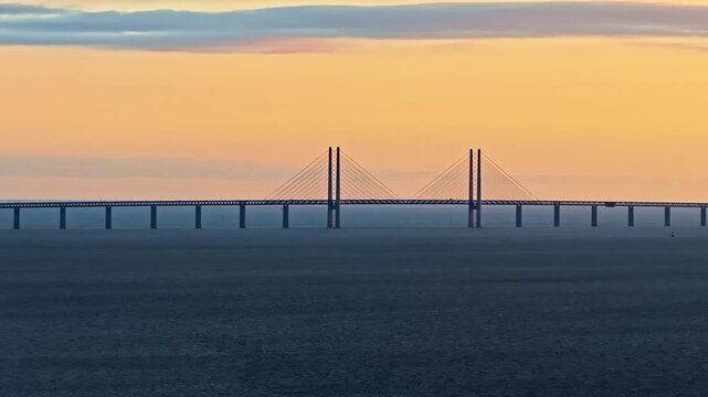 Iconic Oresund bridge connecting Denmark and Sweden over calm ocean at sunset.
