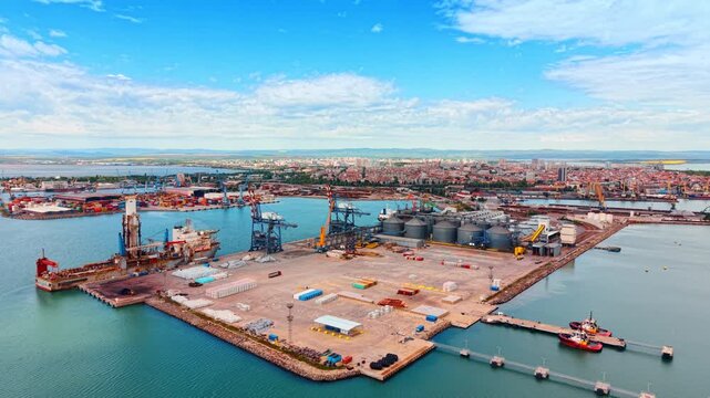 Aerial view of cargo dock with maritime vessel and tugboats. Industrial port terminal featuring specialized maritime vessel, tugboats, and grain silos on concrete pier.