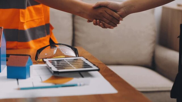 Two engineers are analyzing blueprints and working on a laptop in their office container, discussing the progress of their construction project