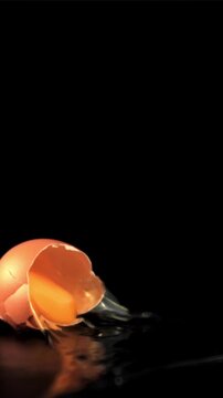 Super slow motion raw egg falls on the table and breaks. On a black background. Filmed on a high-speed camera at 1000 fps.