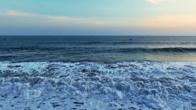 Blue ocean waves rolling toward dark shore