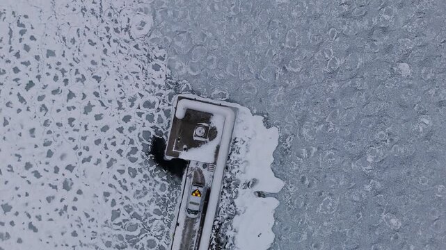 A stunning drone video captures a top-down aerial view of a snowy pier and parked vehicle extending into the frozen waters of Lake V&auml;ttern in J&ouml;nk&ouml;ping, Sweden.