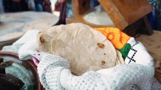 Closeup view of person placing warm corn tortillas onto stack on cloth near hot cooking surface creating authentic traditional food preparation scene