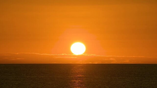 Wide view of sun setting over sea horizon in Padstow Cornwall casting bright orange glow across sky and reflecting on water creating warm peaceful sunset scene