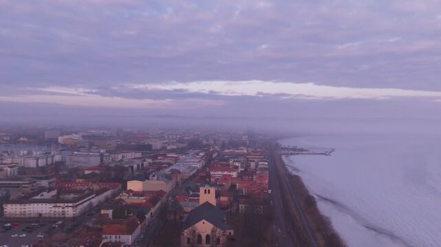 Stunning drone video captures J&ouml;nk&ouml;ping city center and Lake V&auml;ttern coastline at dusk, bathed in rich purple hues. Sweeping aerial footage reveals rooftops, architecture and vibrant sky.