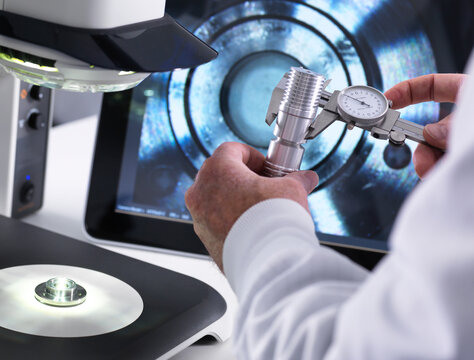 Engineer using a calliper and a 3d stereo microscope for quality control in the manufacturing of engineering components for industry