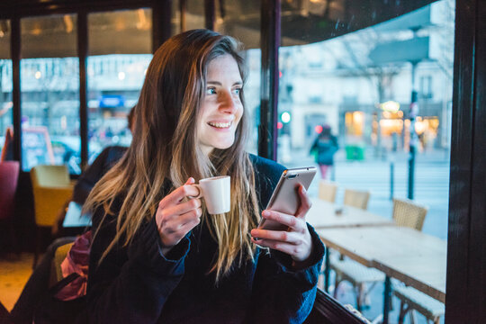 Paris, France, portrait of smiling young woman with smartphone drinking espresso in a coffee shop
