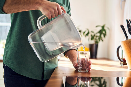 Man pouring water from a filter jug into a glass in the kitchen, close up