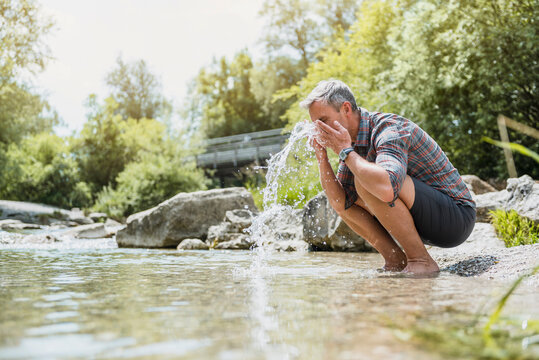 Hiker having a break at the riverbank washing his face