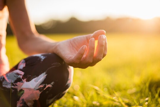 Detail of woman in lotus position on rural meadow at sunset
