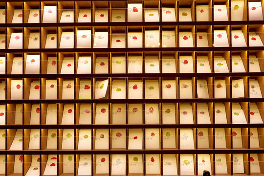Rows of wooden pigeonholes filled with vintage-style envelopes featuring colorful wax seals. Each compartment is labeled with a date. Historic city of Gyeongju, South Korea.