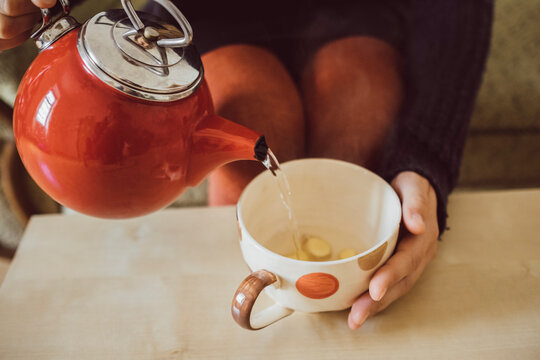 Woman pouring water into tea cup with chopped fresh ginger, close-up