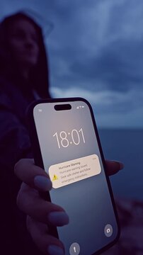 Vertical video. Low Angle Smartphone Hurricane Warning Notification Against Dark Storm Clouds and Ocean Horizon, Climate Risk and Emergency Preparedness