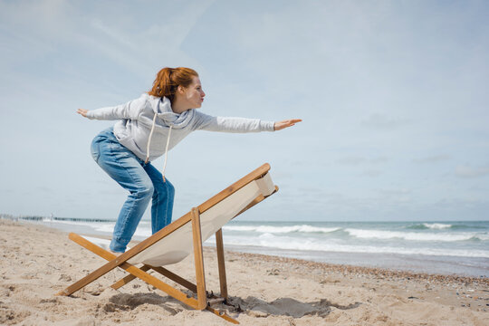 Woman standing on deck chair, pretending to surf