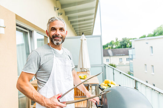 Portrait of smiling man with apron and tongs on his balcony