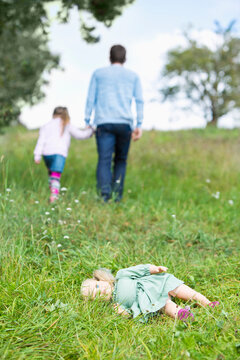 Doll lying on meadow while man going away with little girl