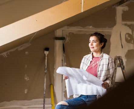 Young woman renovating her new home, holding construction plan