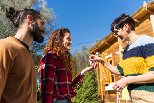 Host welcoming young couple outside a cabin in the countryside handing over house key