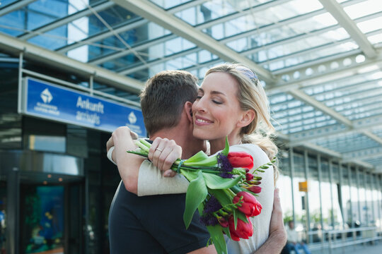 Germany, Leipzig-Halle, Airport, Couple embracing, woman holding flowers