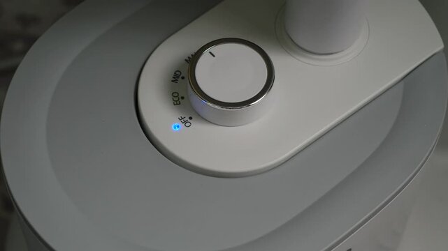 A man's hand smoothly turns a round knob on the control panel to turn off a home appliance. Switching the mechanical dial to the OFF position with a blue LED indicator lighting up