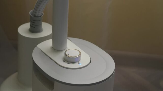 A man's hand turns a mechanical knob to shut down a white garment steamer appliance. Shifting the dial to the OFF position on the control panel of a device emitting a stream of steam