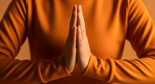 Person in orange shirt with hands in prayer position