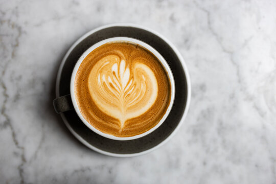 Latte with leaf art in gray ceramic cup on marble surface, top view.