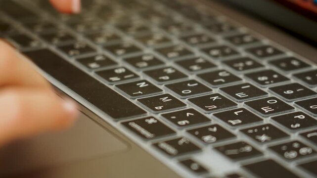 Finger pressing key on backlit Cyrillic and Latin laptop keyboard