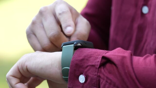 The close up of a man wearing a smartwatch on his left wrist and using this device outside. Electric gadget and a user shot on blurry background.