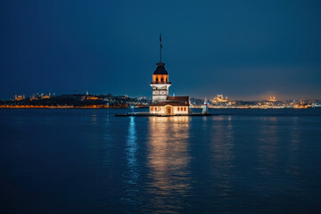 Fototapeta premium Maidenâ€™s Tower in Istanbul creates a captivating evening scene with its illuminated silhouette reflecting over the calm Bosphorus waters.