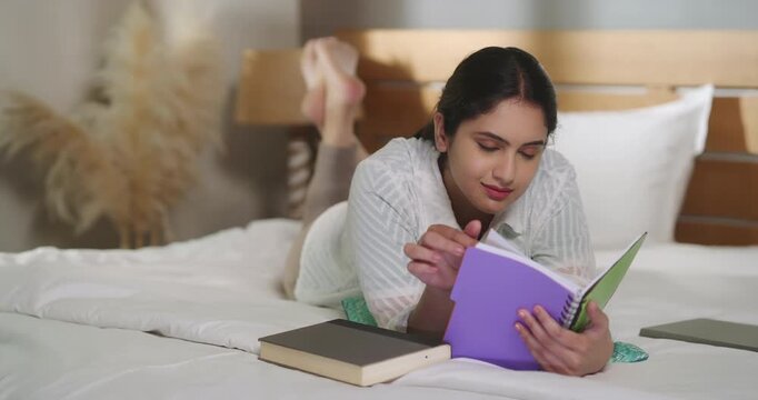 Indian young adult gen z relax calm woman lying on cozy bed read new novel book story indoor room resting girl spend free time do self care enjoy day take break from job work home place