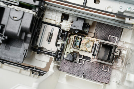Close-up of a printer printhead and internal mechanism showing ink residue, gears and components, illustrating maintenance, repair, cleaning and diagnostic work on office equipment and electronics.