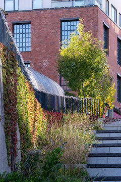 brick facade and stairway define Nordic residential urban architecture, where plants grow beside the railing within a layered courtyard passage