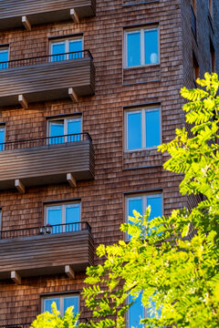 Nordic wood apartment facade in urban residential architecture, where balconies and windows rise behind bright plants along a textured exterior